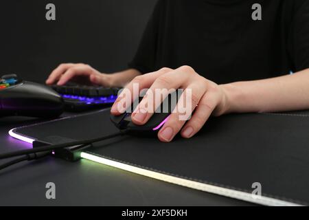 Gamer using modern wired computer mouse at dark table, closeup Stock Photo