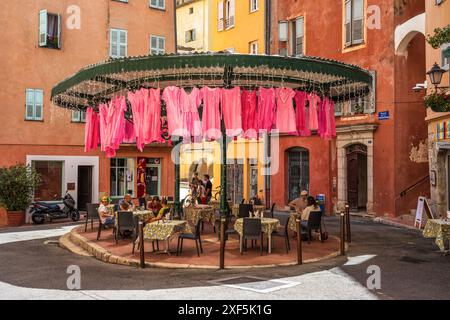 Outdoor café on Place de la Poissonnerie with pink clothes suspended above, in old town of Grasse on the French Riviera, Côte d'Azur, Provence, France Stock Photo