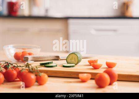 Slicing cherry tomatoes and cucumbers on a wooden table on a kitchen background Stock Photo