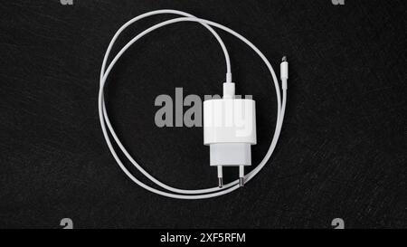 Jurmala, Latvia 25.06.2024: A white Apple lightning charger on black surface with electronics keywords Stock Photo