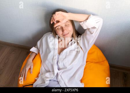 A woman is laying on an orange bean bag chair. She is smiling and she is relaxed Stock Photo