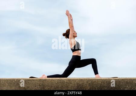 Sporty woman doing a low lunge yoga pose, outside. Stock Photo