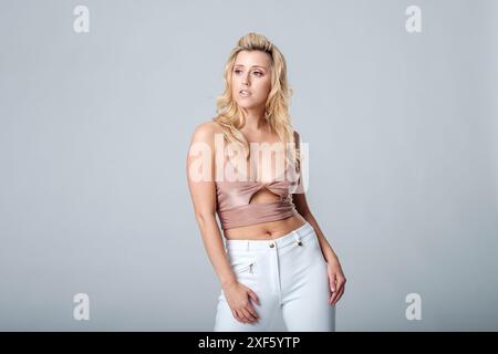 Beautiful blonde fashion model in white jeans and strappy top poses for a shoot in a studio Stock Photo