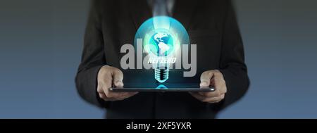 A businessman in a suit holds a tablet with a glowing light bulb icon featuring the Earth and the words "NET ZERO." This image symbolizes the use of A Stock Photo