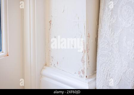 Damp penetration (rising damp) in a solid brick wall causing peeling paint. UK home interior. Stock Photo