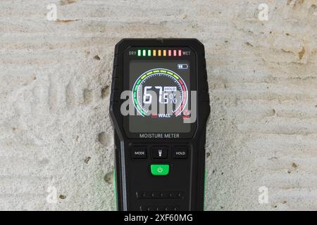 Moisture detector (moisture testing meter) on a concrete floor, reading high moisture content. UK home interior Stock Photo