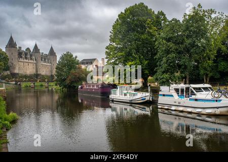 Scenic view of boats docked on the calm Oust River with the historic Josselin Castle in the background, located in Josselin, Brittany, France. Stock Photo