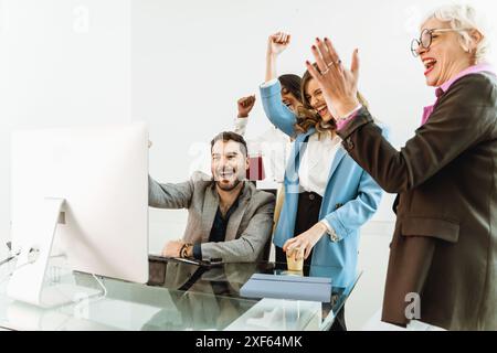 A group of people are celebrating in front of a computer monitor - Coworkers smiling and waving - Scene is happy and celebratory Stock Photo