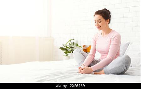 Woman Sitting on Bed With Legs Crossed, Stretching Stock Photo