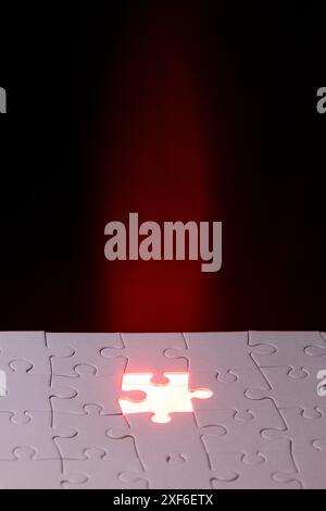 A puzzle piece is missing from a puzzle. The image has a dark background and a bright light shining on the missing piece. Scene is mysterious and intr Stock Photo