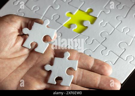 A hand holding two white puzzle pieces with a yellow piece missing. Concept of solving a puzzle and the importance of finding the missing piece to com Stock Photo