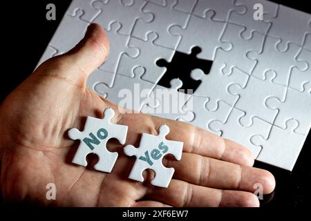 A hand holding three white puzzle pieces with the word "no" and 'yes" written on them. Concept of frustration or disappointment, as the person is hold Stock Photo