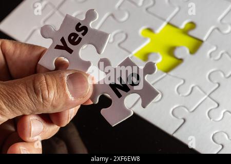 A person holds two puzzle pieces, one of which says "yes" and the other "no". Concept of making a decision or choosing between two options Stock Photo