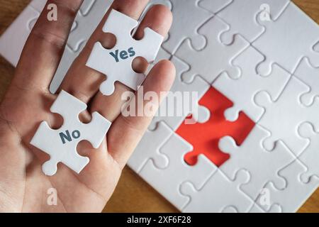 A hand holding two puzzle pieces with the word "yes" on one and the word "no" on the other Stock Photo