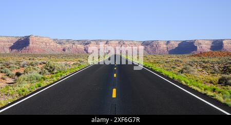 Panorama of desert highway with fresh black asphalt and green lush border leading to red sandstone cliffs in Southern Utah Stock Photo