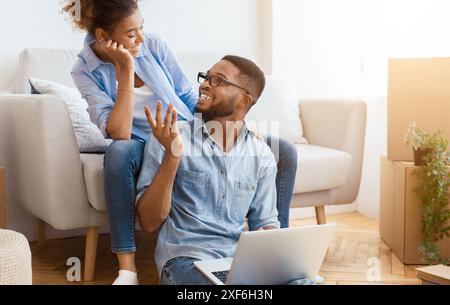 African American Couple Talking Using Laptop Sitting In New Flat Stock Photo