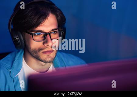 Man Wearing Glasses and Headphones Focuses on Computer Screen Stock Photo