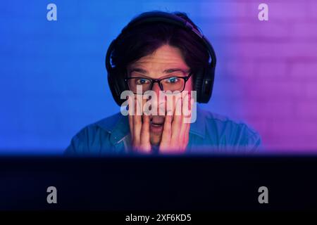 Shocked Gamer In Front Of Computer Screen With Headphones On Stock Photo