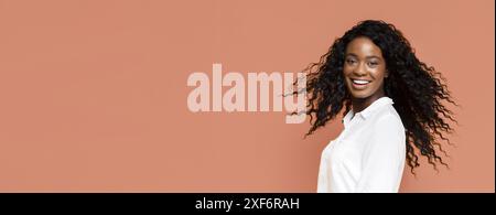 Smiling Woman With Long Curly Hair Against Peach Background Stock Photo