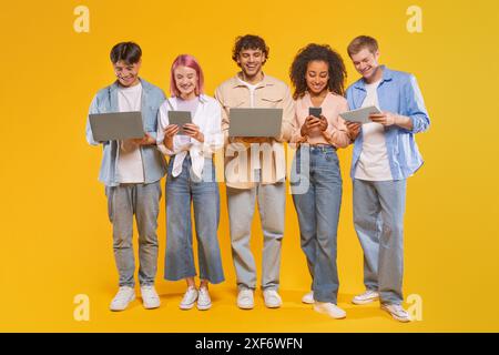 Five Diverse Young Adults Using Technology In Front Of Yellow Stock Photo
