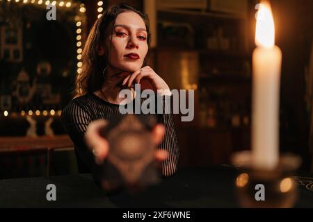 Portrait of mysterious fortune teller asking client to move deck of cards for layout during session, in dark esoteric room by light of burning candle Stock Photo