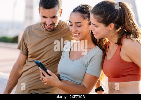 Three young sportive friends using mobile phone after workout routine outdoor Stock Photo