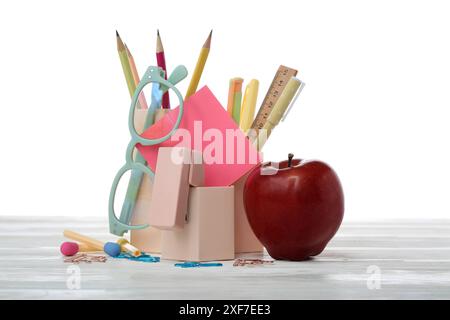 Red apple and school supplies with eyeglasses and sticky notes on table against white background Stock Photo