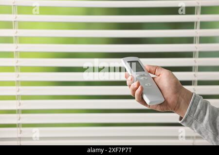 Man using remote control to adjust window blinds indoors, closeup. Space for text Stock Photo