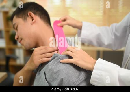 Physical therapist placing pink kinesio tape on man patient shoulder and neck at the clinic office. Alternative medicine concept Stock Photo