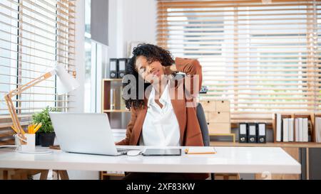 A tired, overworked Black businesswoman is massaging her neck, suffering from office syndrome, experiencing neck pain, and feeling exhausted during wo Stock Photo