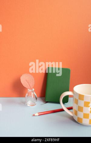Workspace object. Notebook, colored pencil, vase of plant, mug cup on gray desk. red wall background Stock Photo