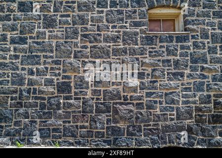 A small arched window in an exterior stone wall of an old building Stock Photo