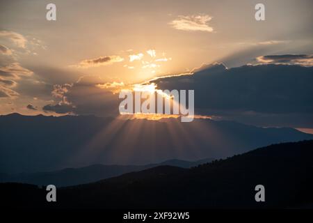 Bright sunlight shining through hole of clouds to dark scene of mountain range before sunset in Bulgaria. Stock Photo