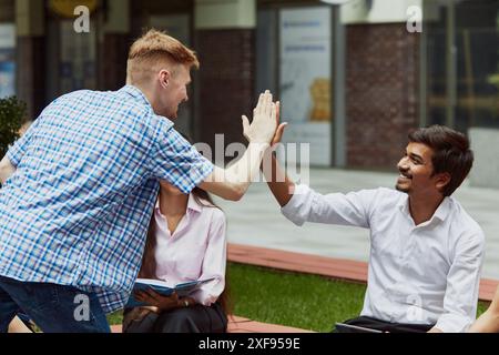Hello. Caucasian young guy giving high five to Indian friend. Multicultural students meeting outdoors the campus for common studying Stock Photo
