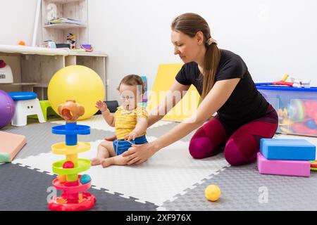 Physiotherapist assisting a little child with coordination disorders during motor skills development exercise in modern rehab clinic. Physiotherapy Stock Photo