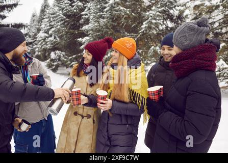 Happy friends with hot drinks in paper cups chatting and having fun outdoors in winter park. Stock Photo