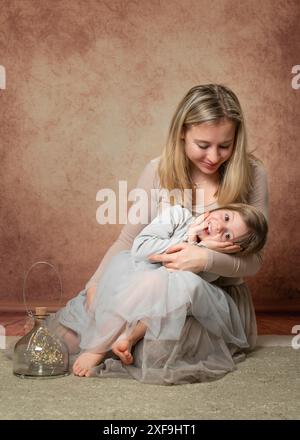 A young mother tenderly looks at her little daughter. The girl laid her head on her mother's lap. Family portrait. Love, care, tenderness. Studio shoo Stock Photo