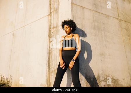 Woman resting and breathing after a runnning session, leaning against a concrete wall in an urban setting, wearing athletic clothing. Stock Photo
