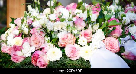 Chrysanthemum Rosa funeral flowers of pink roses and white chrysanthemums on a base of fir branches on a grave with a wooden cross in the background Stock Photo