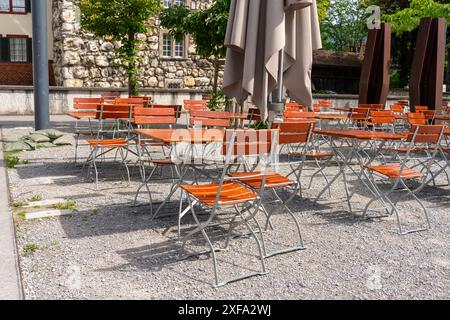 Empty tables at the outside in front of a cafe on a sunshiny day are inviting people to sit down and have a rest and a drink or food. In the backgroun Stock Photo