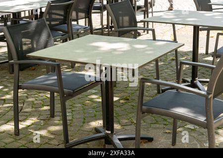 Close up view of a table with two chairs on the street, close to a cafe. Some sunlight seeping through the trees and creating a light pattern on the t Stock Photo