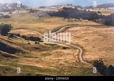 Rural scene of dirt road through golden dry hill on wilderness in farmland Stock Photo