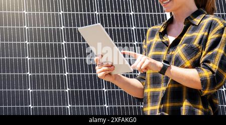 A female engineer works on a digital tablet in front of a solar panel at a solar power plant. Stock Photo