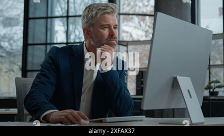Mature focused thoughtful caucasian businessman marketing specialist working on computer in office man entrepreneur manager thinking analyzing finance Stock Photo