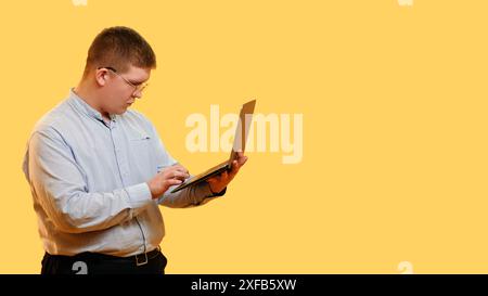 Internet work. Program developer. Search of information. Smart busy overweight man using laptop touching keyboard isolated on yellow empty space background. Stock Photo