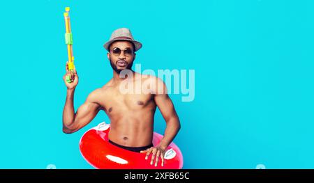 Man Holding Water Gun Wearing Hat Against Blue Background Stock Photo