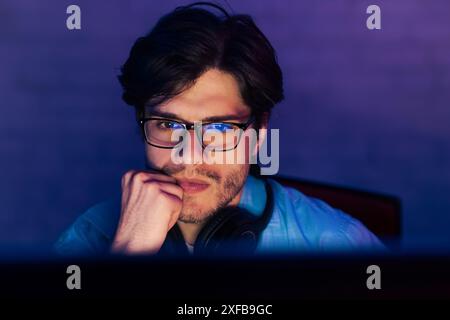 Young Man Wearing Glasses Works On Computer in Dark Room Stock Photo