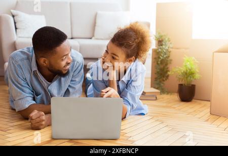 Spouses Using Laptop Lying On Floor Among Moving Boxes Indoor Stock Photo