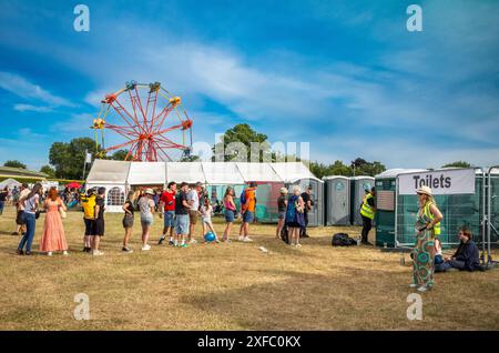 Guildford / UK - Jun 29 2024: People queue for the toilets near a ferris wheel at Guilfest music festival, Guildford, Surrey, UK. Stock Photo