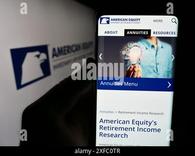 Person holding cellphone with webpage of American Equity Investment Life Holding Company in front of logo. Focus on center of phone display. Stock Photo